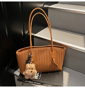 Détail d'un sac cabas marron tissé avec poignée en cuir nouée et charm chiot en peluche
