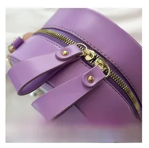 Detail of smooth gold double zipper and purple leather texture on round crossbody bag