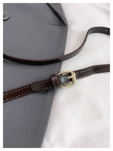 Detail of dark brown leather strap with polished gold buckle on grey blazer suit fabric