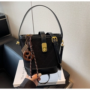 Detail of black quilted bucket bag with golden hardware and a pretzel-shaped charm detail