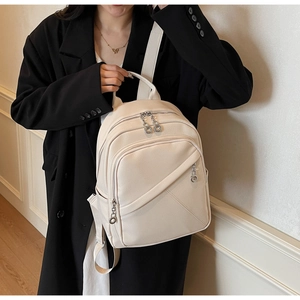 Detail of cream pebbled leather backpack showing diagonal zip pocket and metal hardware