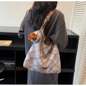 Detail of grey retro checkered tote bag with brown leather strap and plush monster charm
