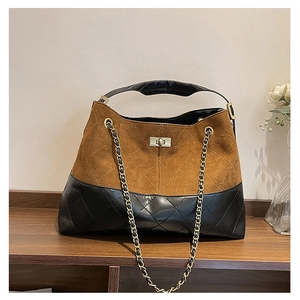 Detail of suede and quilted leather patchwork bag with gold chain strap on wooden shelf