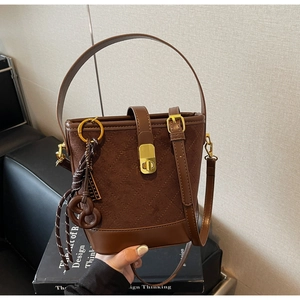 Detailed close-up of dark brown quilted suede bucket bag with gold clasp and pretzel charm
