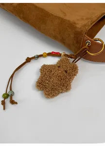 Close-up of star-shaped plush charm with colorful beads and bell on a suede tote bag