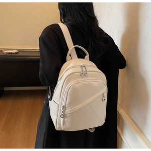 Minimalist beige backpack with litchi texture shown on model in black suit
