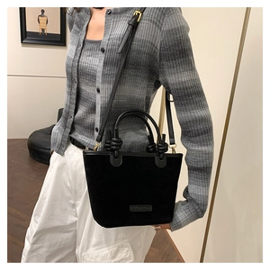 Detail of black suede bucket bag with knotted handle and metallic logo on the bottom
