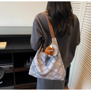 Detail of grey quilted hobo bag with wide brown strap and decorative plush pendant