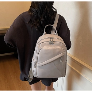 Rear view of a light gray leather backpack worn by a model in a minimalist indoor hallway