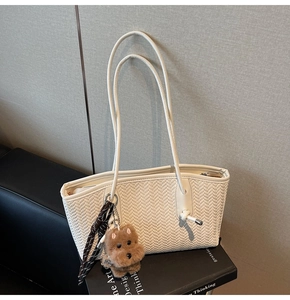 Détail du cabas blanc tressé avec un pendentif chiot en peluche et des glands tressés