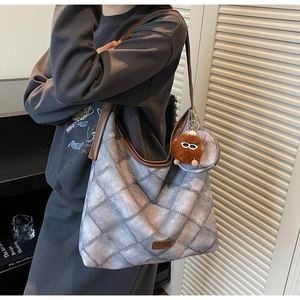 Detail of grey quilted tote bag with brown straps and plush toy charm on model