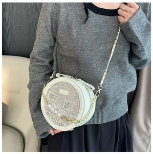 Detail of round beige crossbody bag with pearl chain strap and woven texture