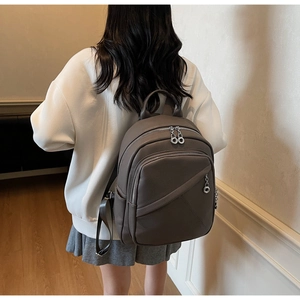 Detail of dark taupe pebble leather backpack showing silver ring zippers on model