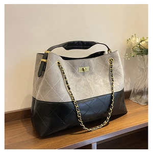 Detail of quilted suede tote with grey and black patchwork, metal lock, and chain strap