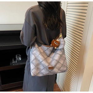 Quilted gray tote bag with leather strap and plush monster charm in minimalist setting