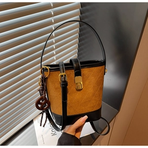 Detail of brown suede bucket bag with quilted patterns and a pretzel charm accessory
