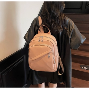 Detail view of beige pebbled leather backpack with multiple silver zippers on a model