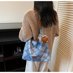Detail of blue quilted denim tote bag featuring brown strap and cute plush monster charm