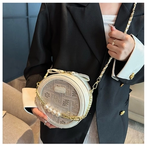 Detail of round off-white crossbody bag with embroidery, pearl chain, and bow accent