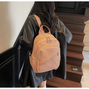 Detail showing the light brown lychee grain leather texture and silver zippers on backpack