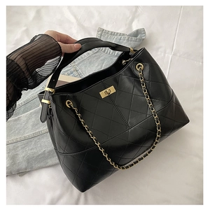 Detailed shot of black quilted faux suede tote bag with gold metal twist lock and chain