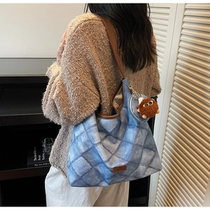 Detail of blue quilted tote bag with brown leather straps and plush monster charm