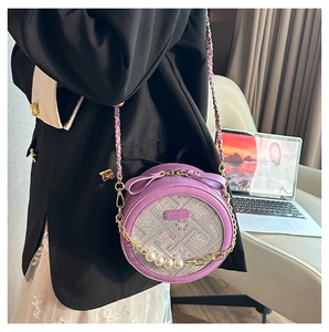 Detail view of purple round crossbody bag with pearl chain shown on a black blazer outfit