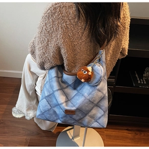 Detail of blue denim tote bag with brown leather trim and plush charm worn by model