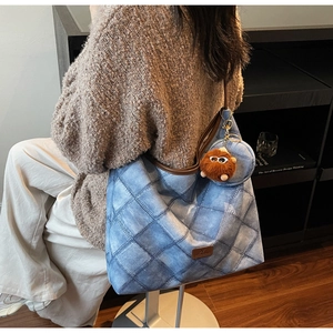 Detail of blue denim quilted tote bag with brown leather handles and plush monster charm
