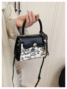 Close-up of contrast color handbag featuring vintage landscape art and golden floral clasp