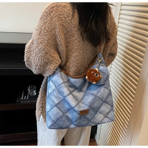 Detail of blue denim quilted hobo bag with brown trim and plush pompom charm