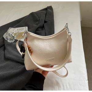 Detail of cream half-moon underarm bag featuring wooden bead charm and leather texture