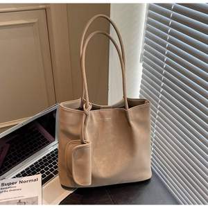 Detail of a large beige tote bag with a small accessory pouch next to a laptop