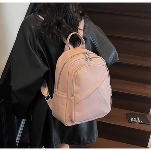 Detail of pink faux leather backpack with litchi texture and metal zippers shown on model