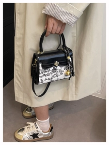 Close-up of ink wash painting pattern handbag with golden floral clasp and striped scarf