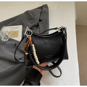 Detail of black leather crossbody bag with beaded tassel charm on a stylish suit background