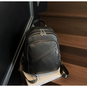 Detail of black pebbled leather backpack with silver zippers on a wooden staircase