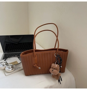 Gros plan détaillé du sac cabas marron tressé avec breloque d'ours sur un bureau blanc
