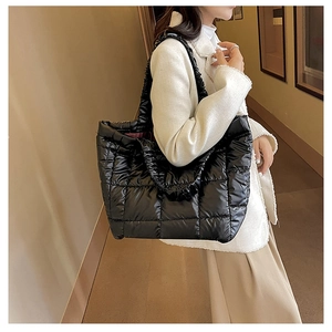 Side view of a black quilted puffer tote bag with glossy nylon texture and padded straps