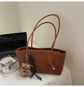 Détail d'un sac cabas tressé marron avec anses à nœuds et charm de chien en peluche