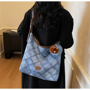 Detail of denim blue quilted tote bag with brown leather strap and plush charm