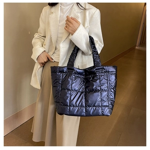 Deep blue quilted tote bag with metallic finish and ruffled handles worn by a model