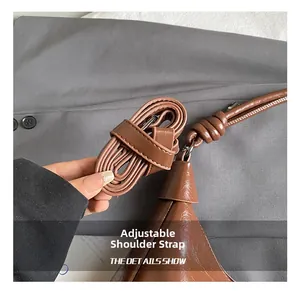 Detail of adjustable strap on brown PU leather bag with white stitching and metal buckle