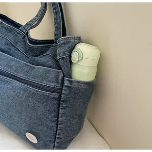 Detail of denim tote bag showing side pocket with water bottle and front zip pocket