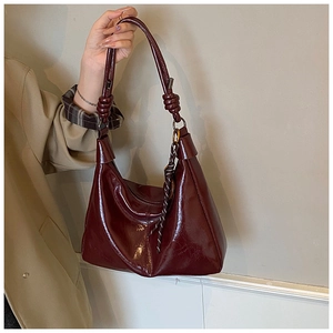 Detail of burgundy glossy hobo bag with knotted strap and decorative silk scarf