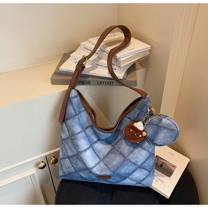 Detail of blue quilted denim hobo bag with brown strap and plush bear keychain accessory