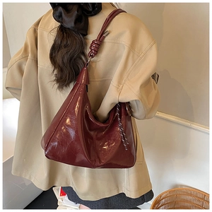 Side view of a burgundy glossy leather tote bag with a unique knot strap detail