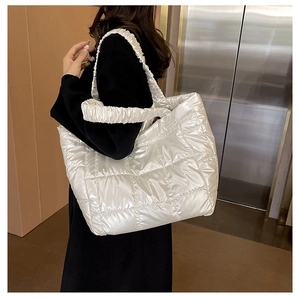 Close-up of white quilted tote bag with ruffled handles and glossy metallic finish
