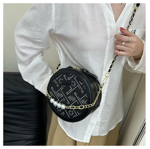 Detailed view of embroidery pattern and pearl chain on a black circular crossbody bag