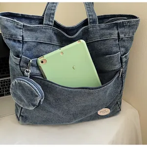 Detail of blue denim tote bag featuring a front zipper pocket with green tablet inside